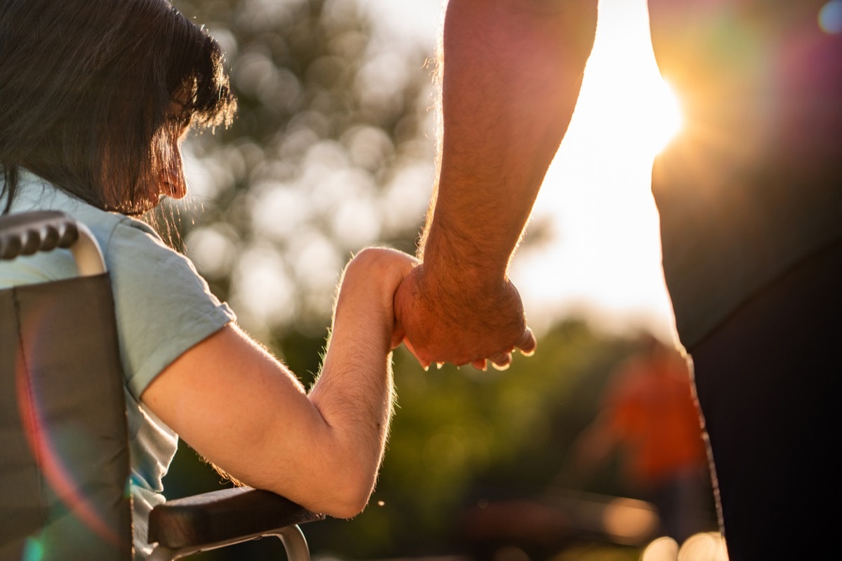 Close up of a woman in a wheelchair holding a man's hand