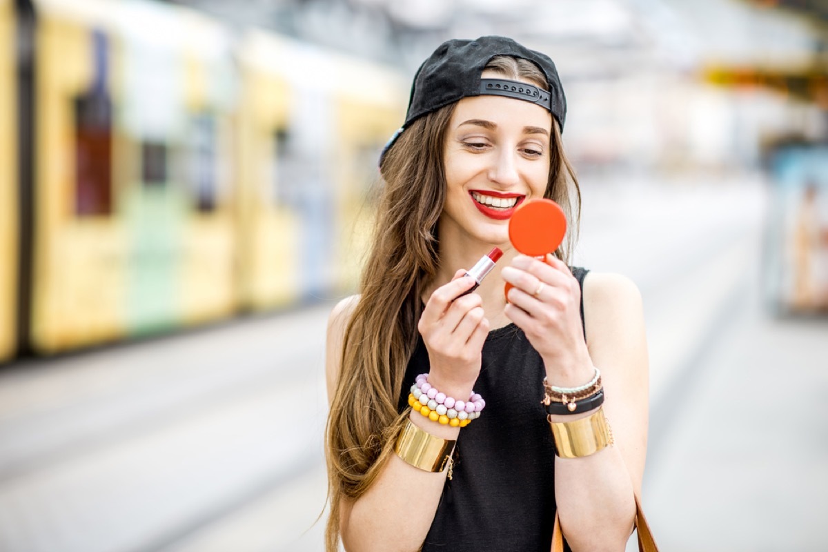 hipster woman applying red lipstick outdoors, summer beauty products