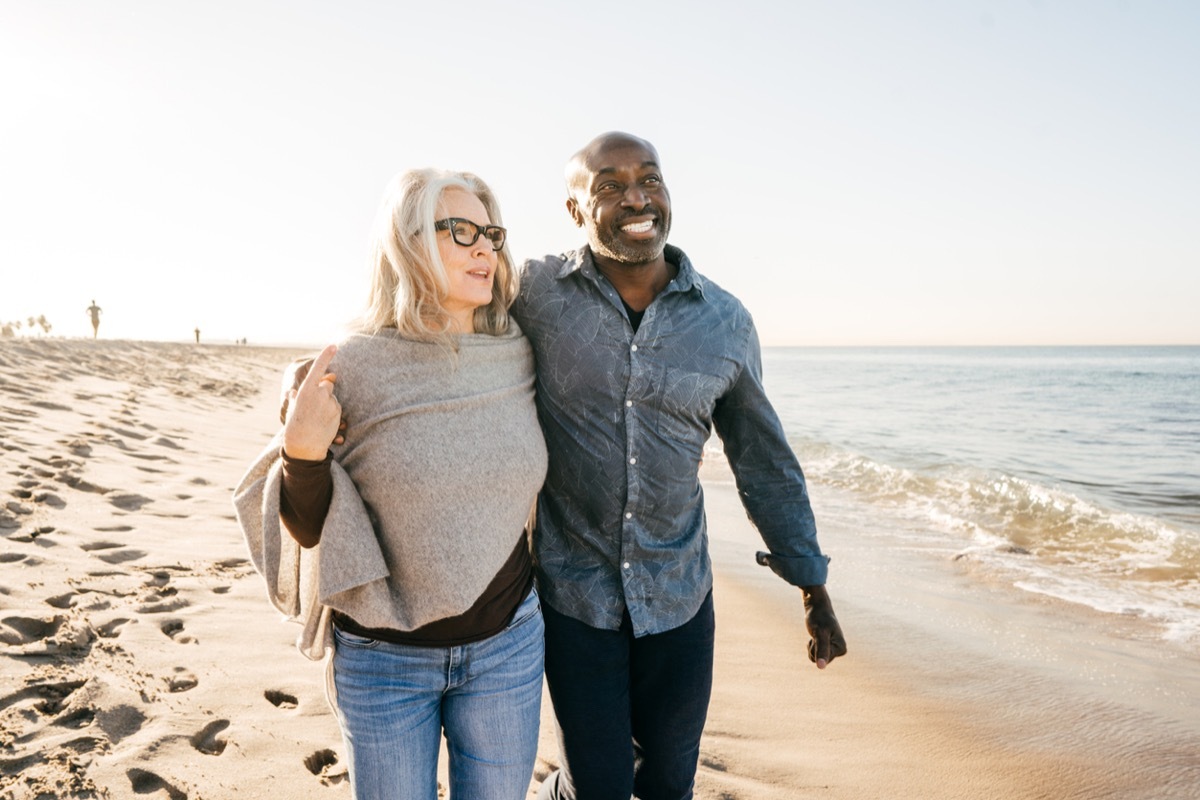 older white woman black man couple walking on the beach with their arms around each other