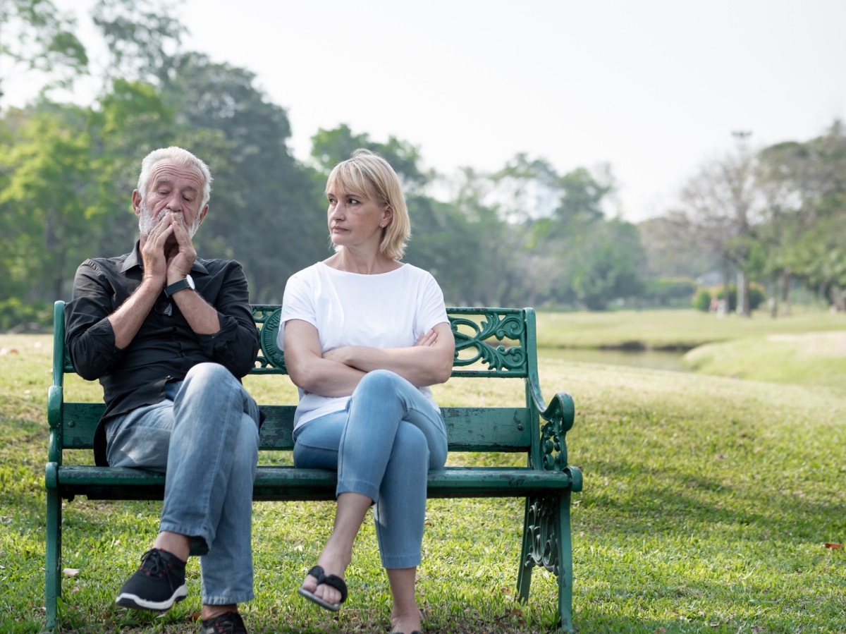 Senior couple having problems in the park, both have legs crossed