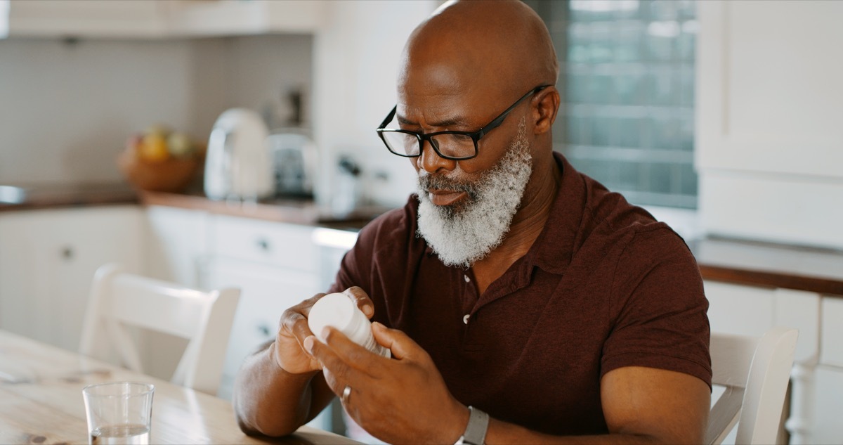 Cropped shot of a senior man sitting alone in his kitchen and taking pills