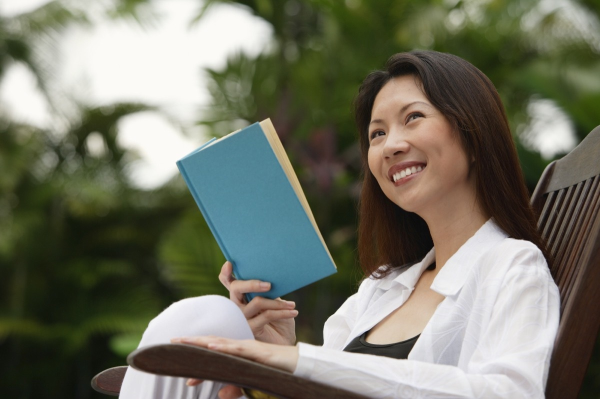 30-something asian woman reading a book outdoors