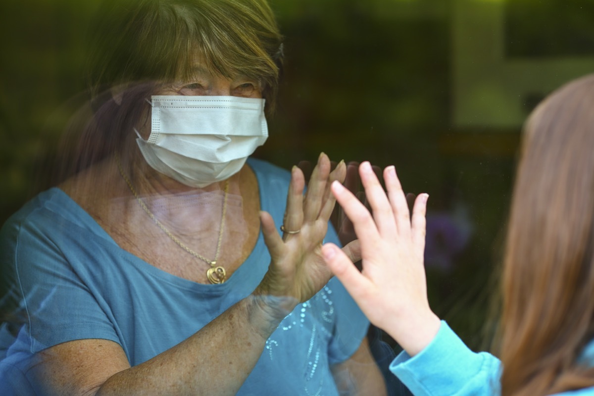 Grandmother and granddauther touch hands on window while on visit. Senior woman staying at home in time of quarantine for coronavirus or Covid-19. Lockdown visit of a senior adult.