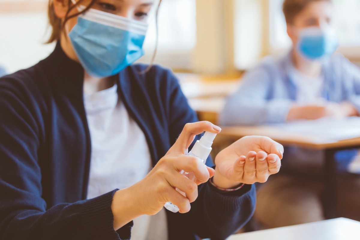 School students wearing N95 face masks and using hand sanitizer. Sitting in a classroom. Close up of hands.