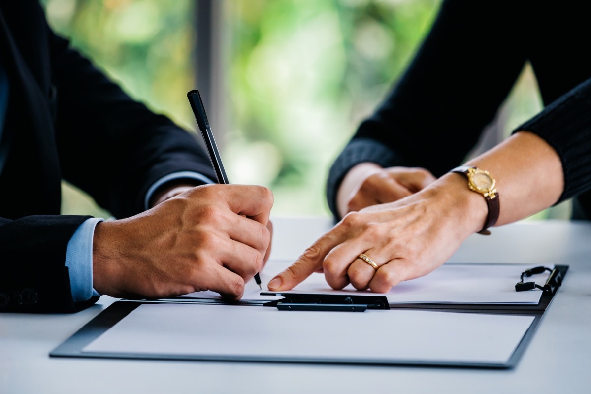 Side view of crop businesswoman pointing at contract to businessman with pen at table at office