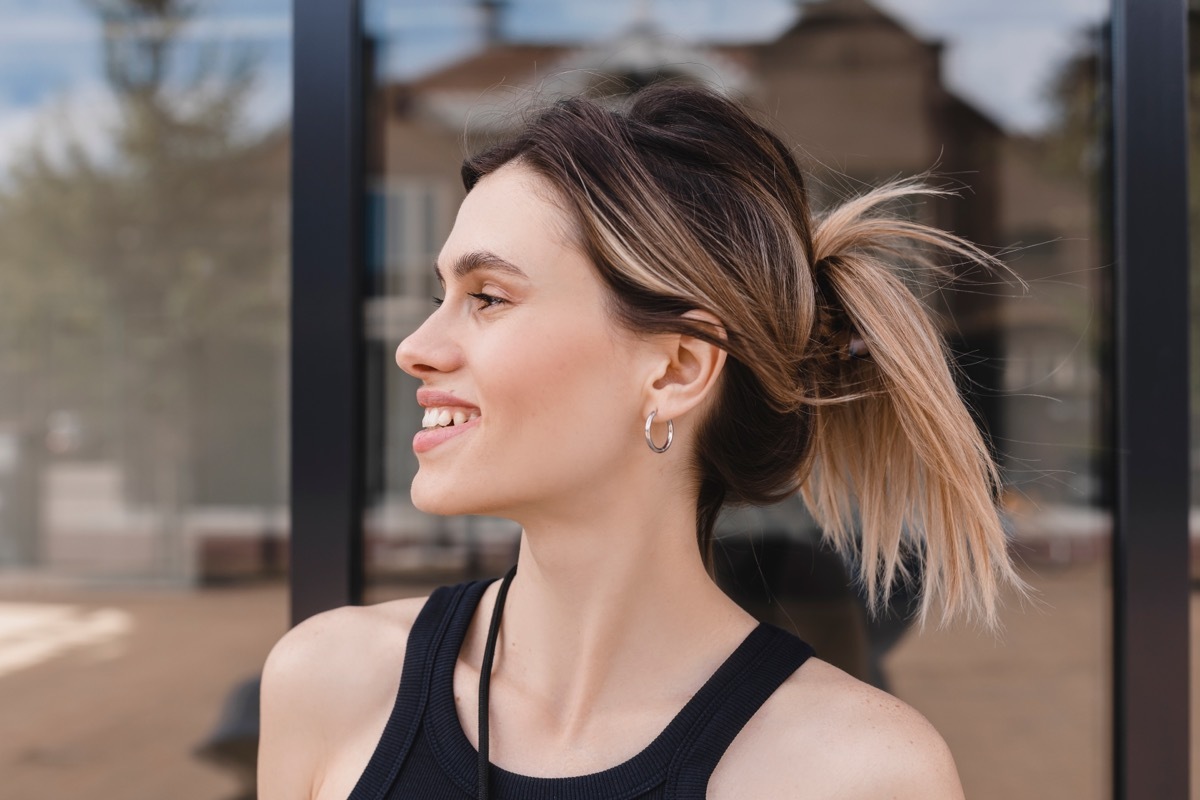 Close-up portrait shot of a young blonde business lady with a hair claw in her straight hair. Woman standing near business centre building and look at side with a style hairstyle, earrings.