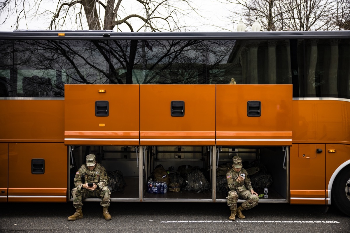 national guard members sitting in cargo hold of orange bus