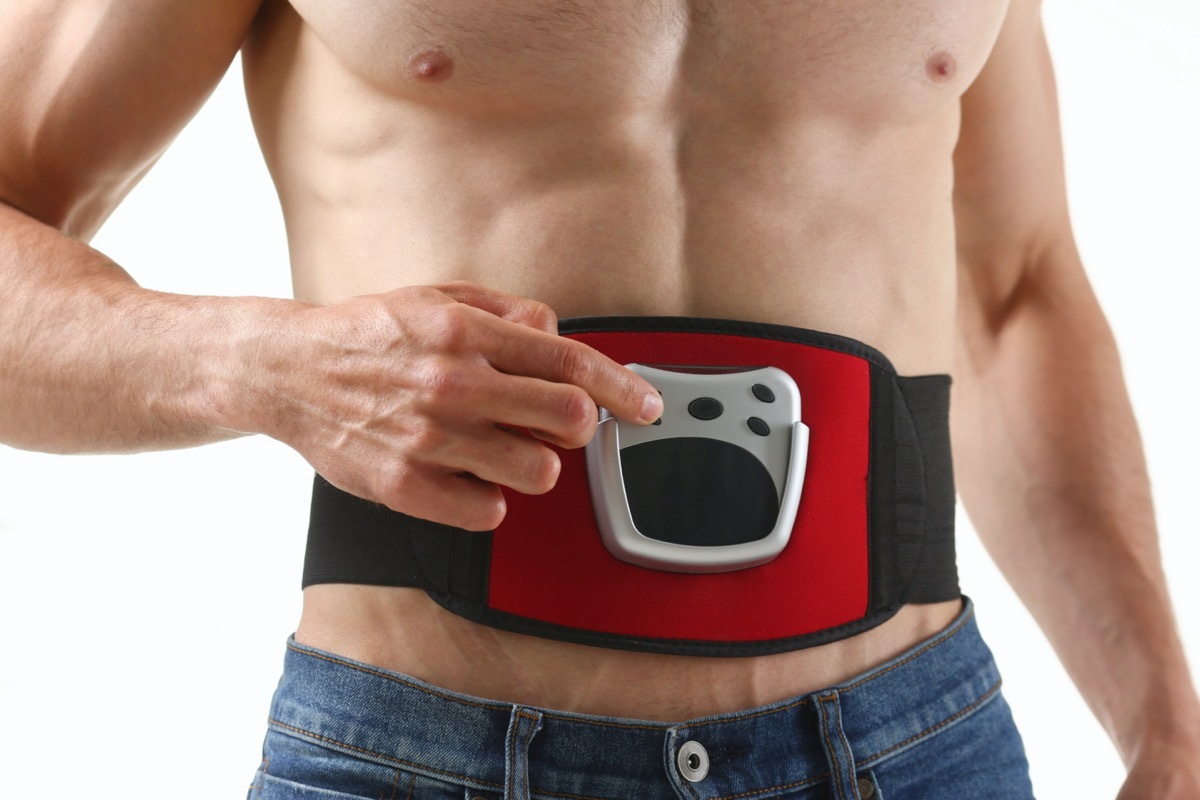 Athletic folded man uses an electric belt simulator for training a press