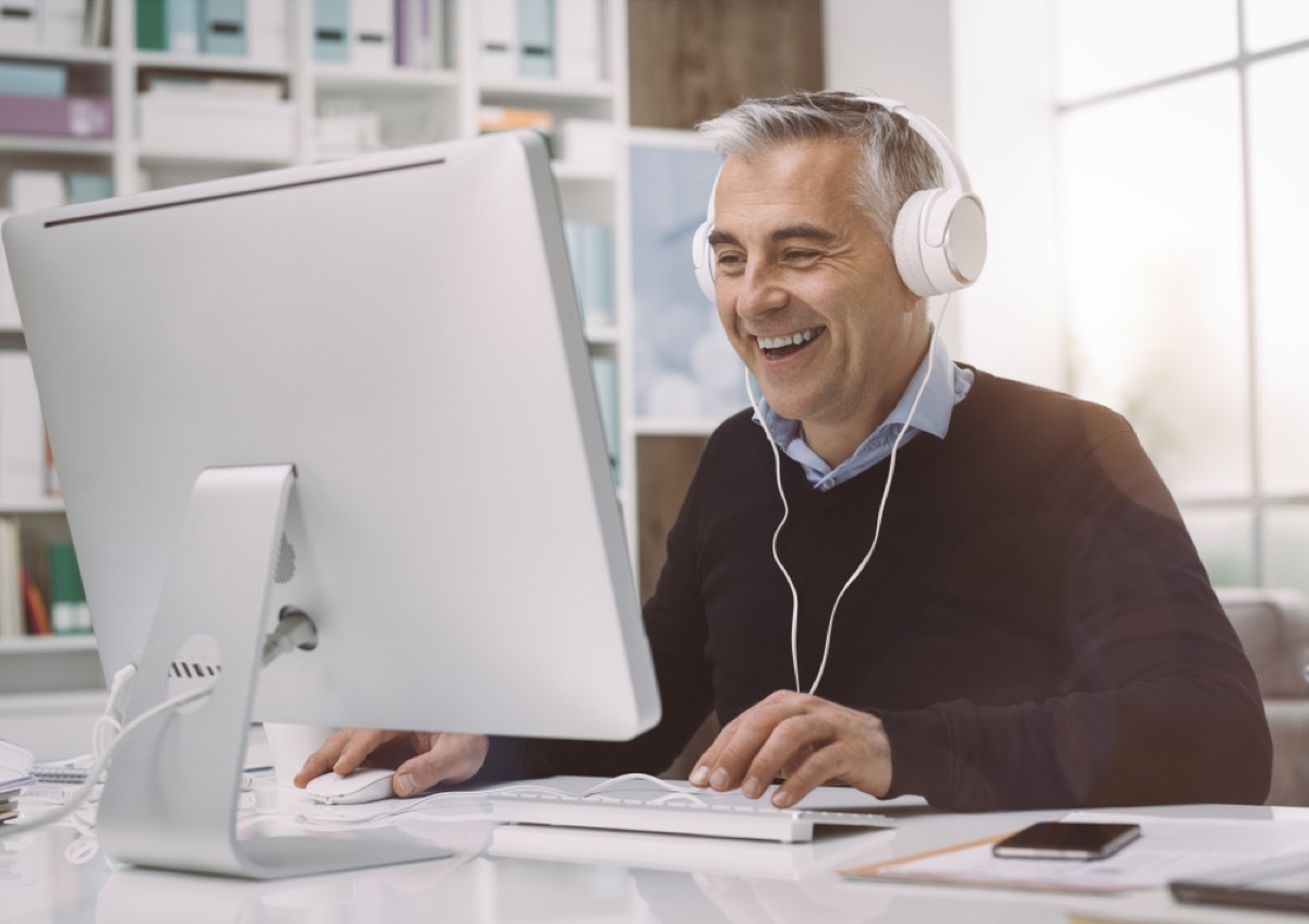 older man with gray hair wearing headphones at his desk, office etiquette