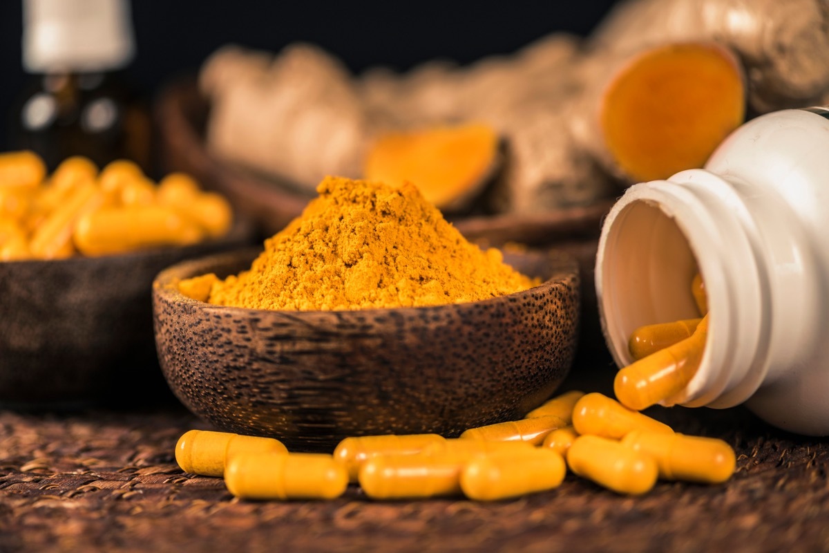 Curcumin supplement capsules, turmeric powder in glass bowl and curcuma root in background.