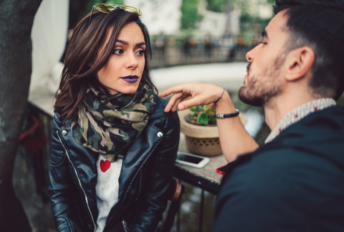 white woman looking off in the distance while white man talks to her at outdoor cafe