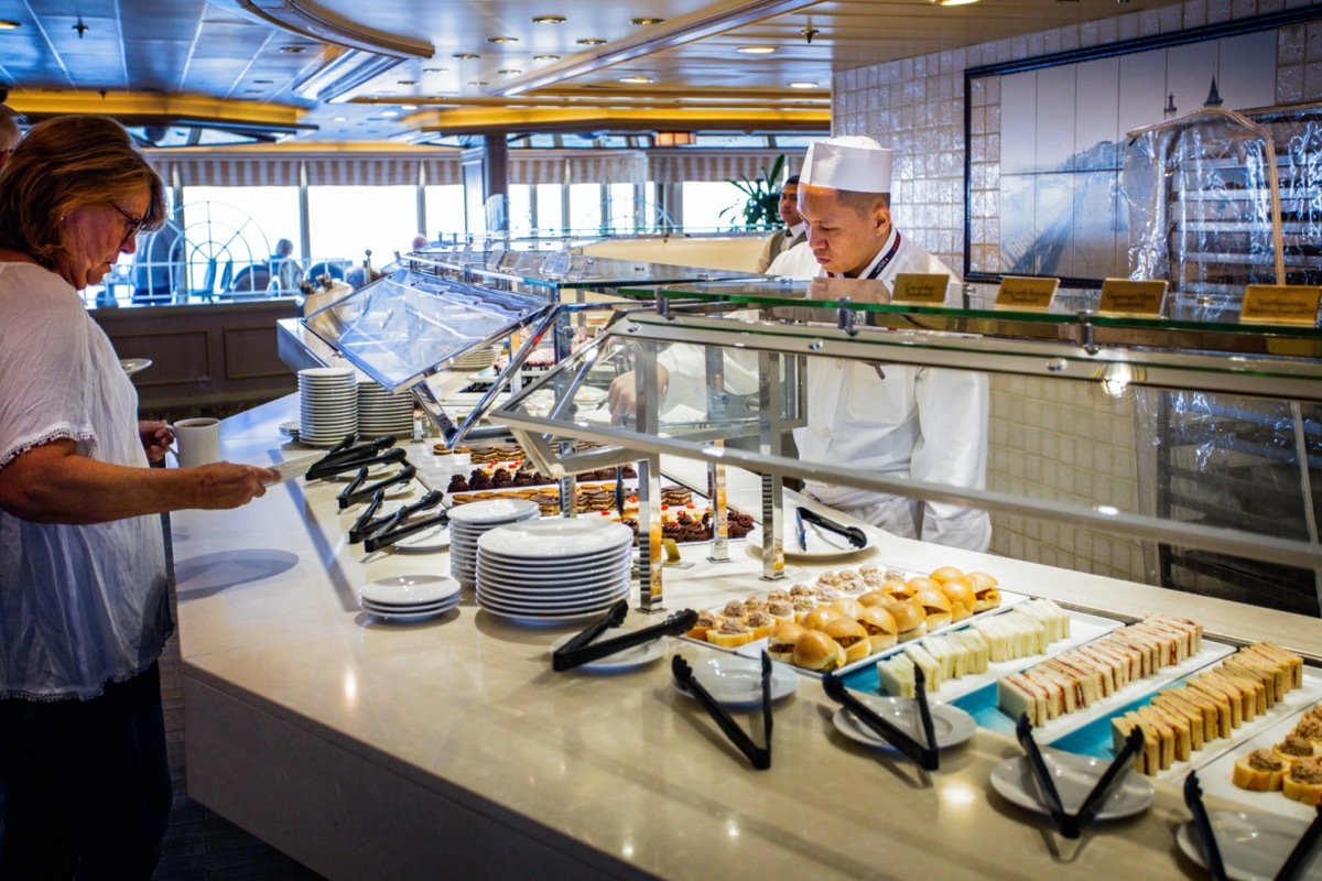 a woman puts food on her plate in a cruise ship buffet line