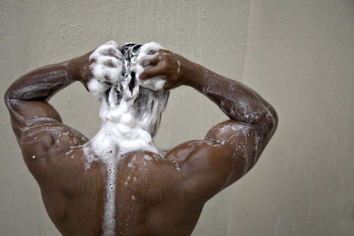 black man with his back to camera shampooing his hair in the shower