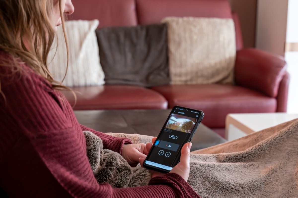 Brilon, North Rhine Westphalia / Germany - January 31st 2020: A woman is lying on the couch. She looks at cell phone. Display shows shot of the surveillance camera ring from Amazon.