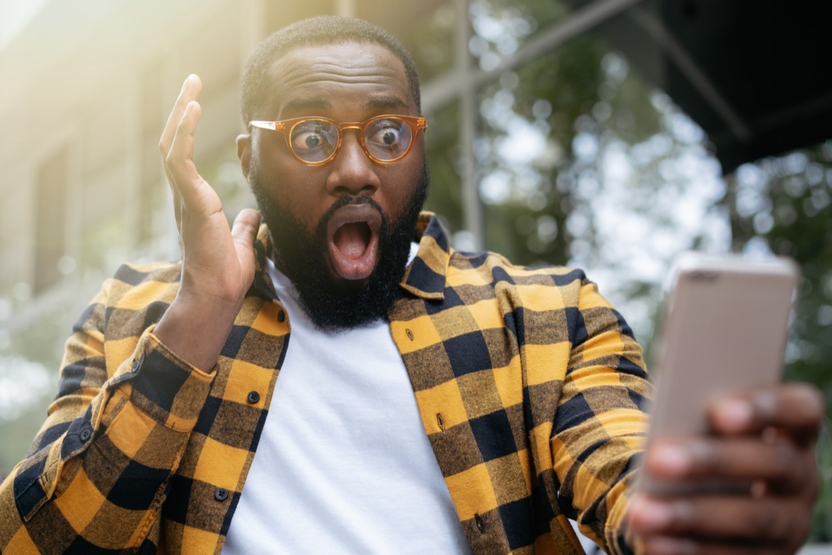 young man looking at his phone with his mouth open learning about emoji meanings