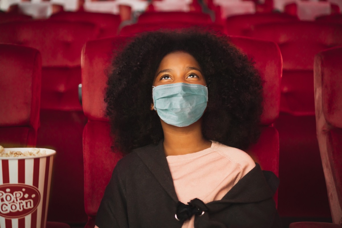 Girl wearing mask in movie theater seat