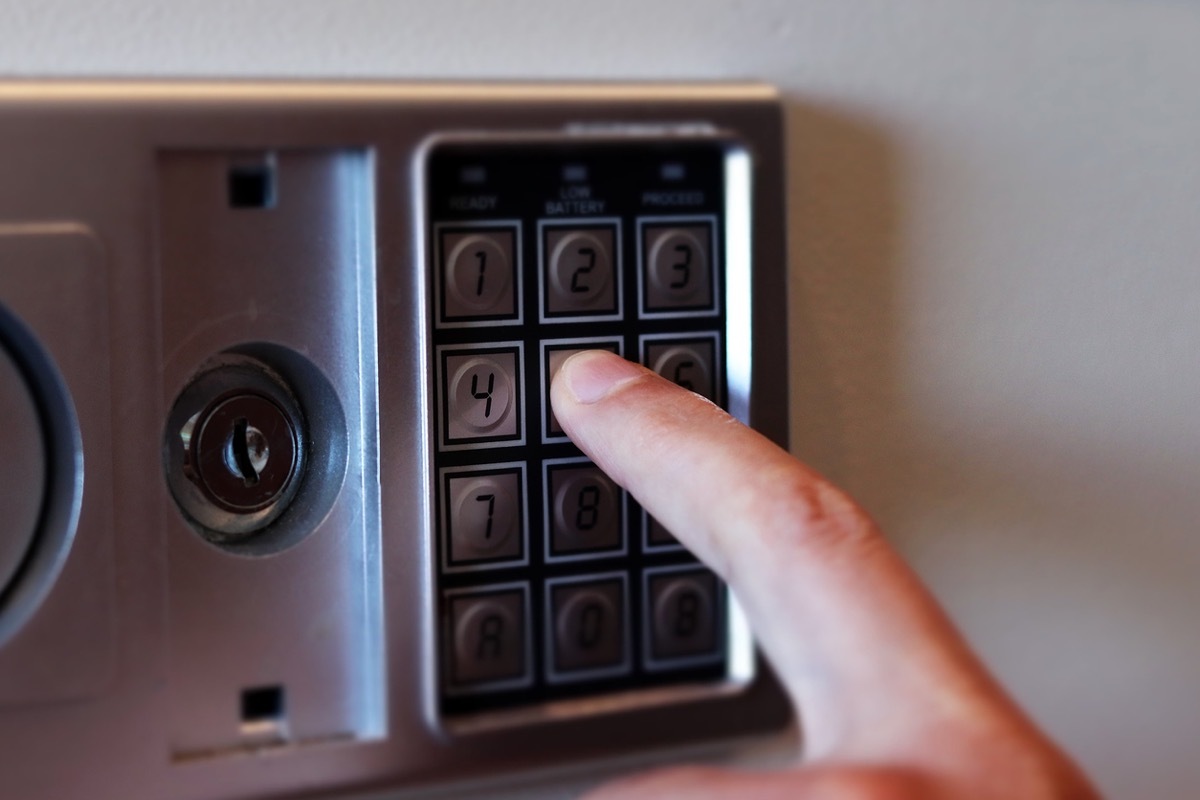 Blurred safe with combination lock and human hand in a hotel room, closeup numbers with tilt shift effect. Selective focus.