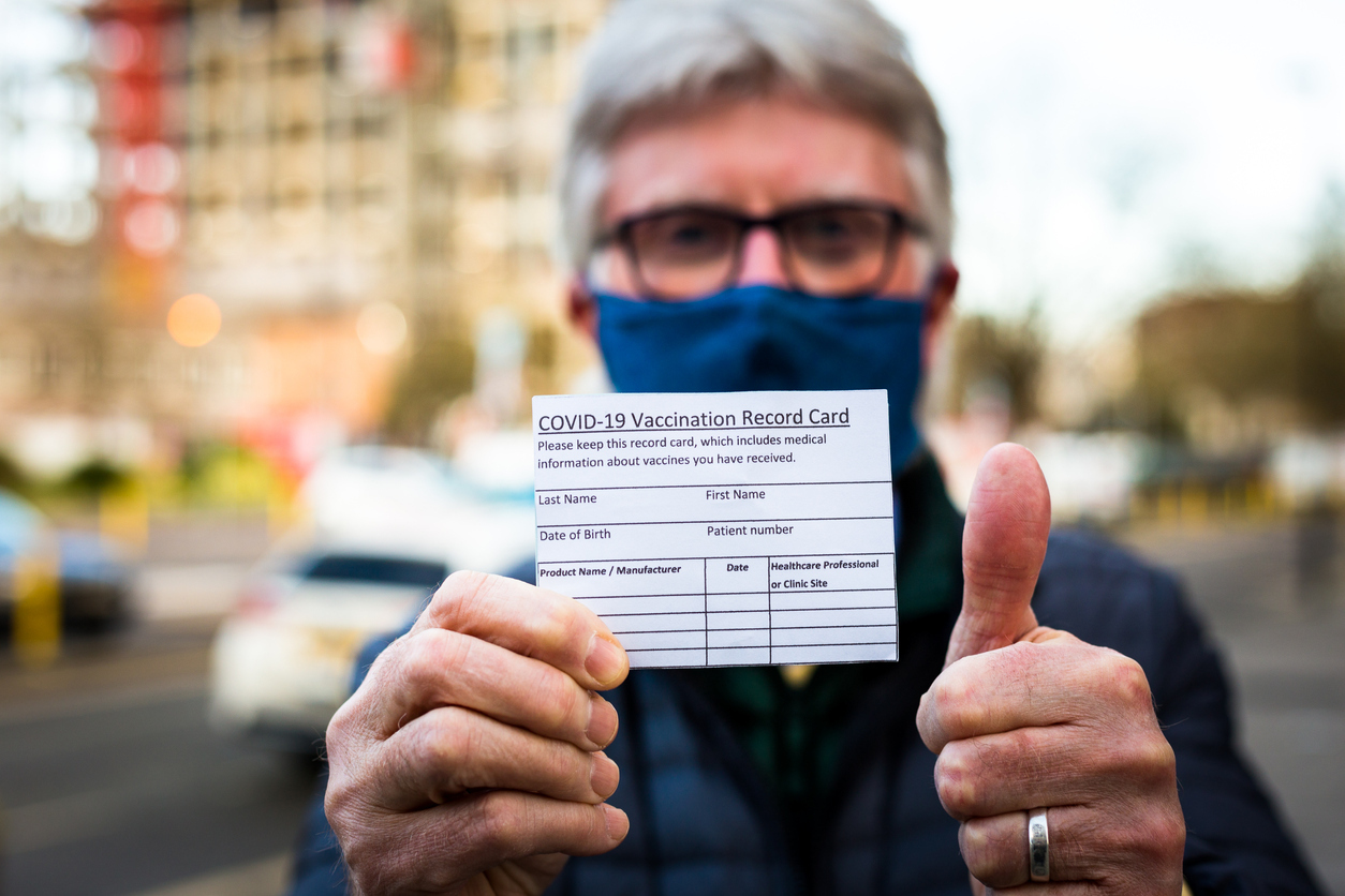 A man holding his COVID-19 vaccination record card while giving a thumbs up