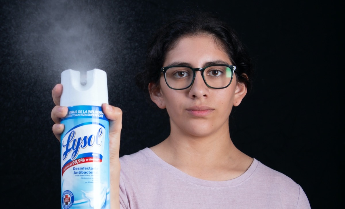 Woman disinfecting room with Lysol spray that kills germs during coronavirus (COVID-19) global pandemic