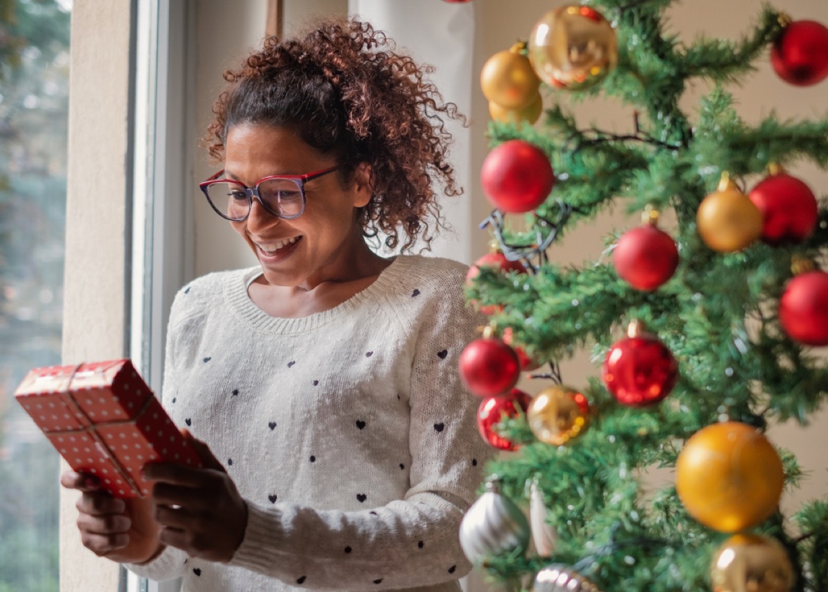 young black woman holding gift in front of christmas tree