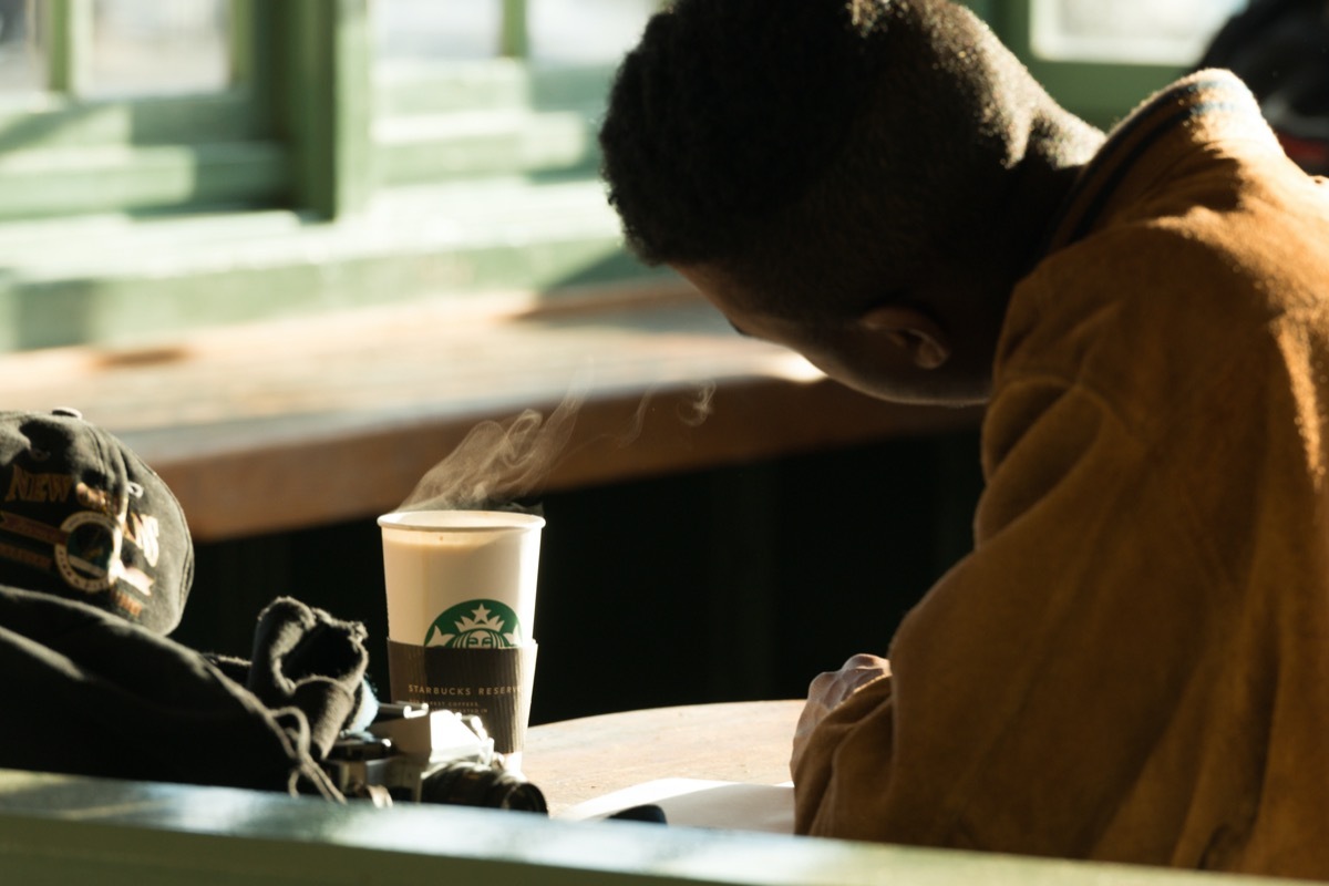 A man In Pike Place Market late in the day with a hot cup of Starbucks coffee.