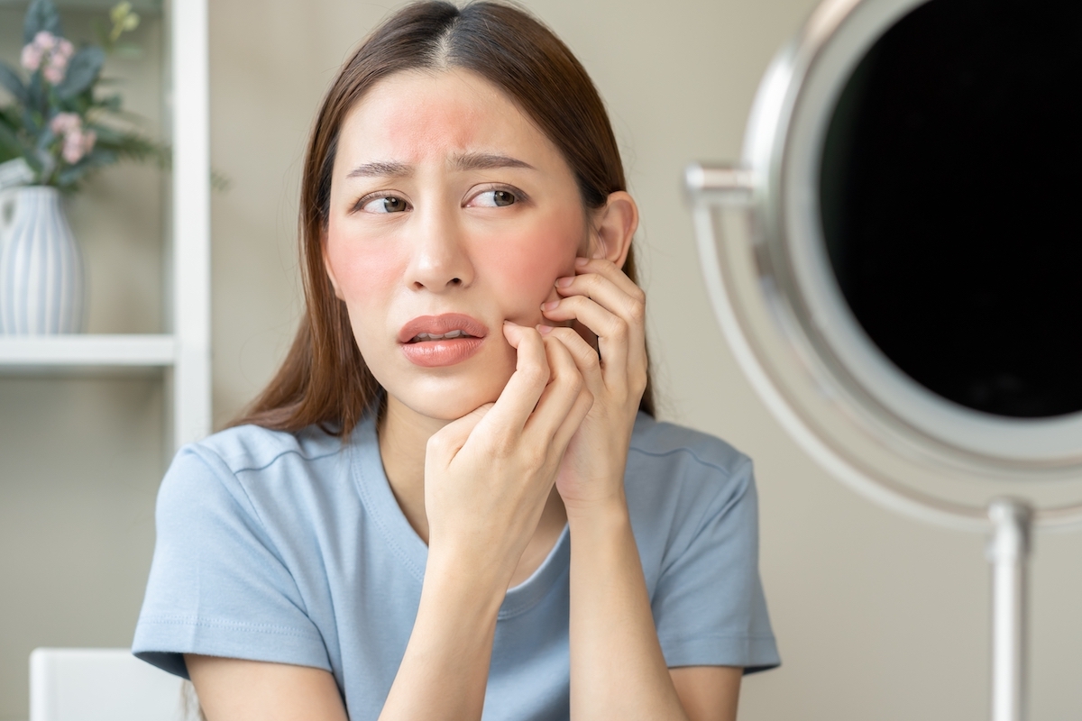 A young woman looking in the mirror at a rash on her face.