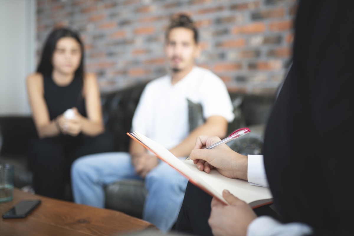 Young couple having session with psychologist at office. Psychologist is talking about problems. Young couple is listening to her.