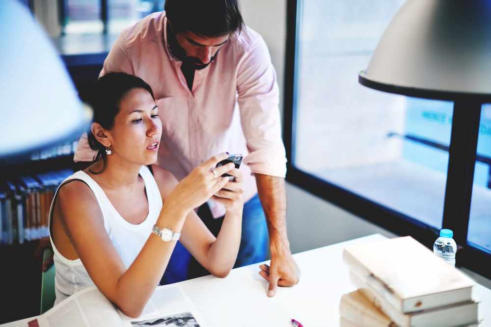 A woman using an Android smartphone while a male colleague watches over her shoulder