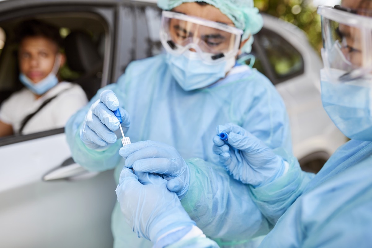 Doctor taking coronavirus sample from male patient. Frontline workers are in protective workwear. They are standing by car during epidemic.