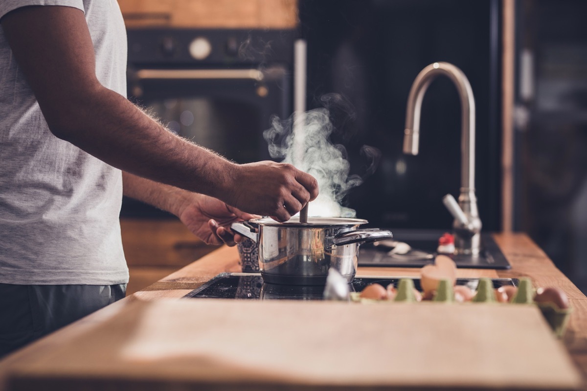 Unrecognizable man stirring soup in a saucepan while making lunch in the kitchen.