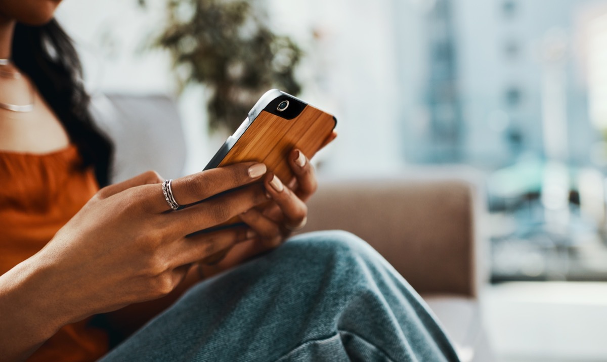 Cropped shot of a woman using a smartphone while relaxing on the sofa at home