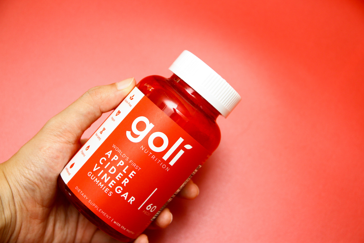 A hand holding a bottle of Goli apple cider vinegar gummies on red background