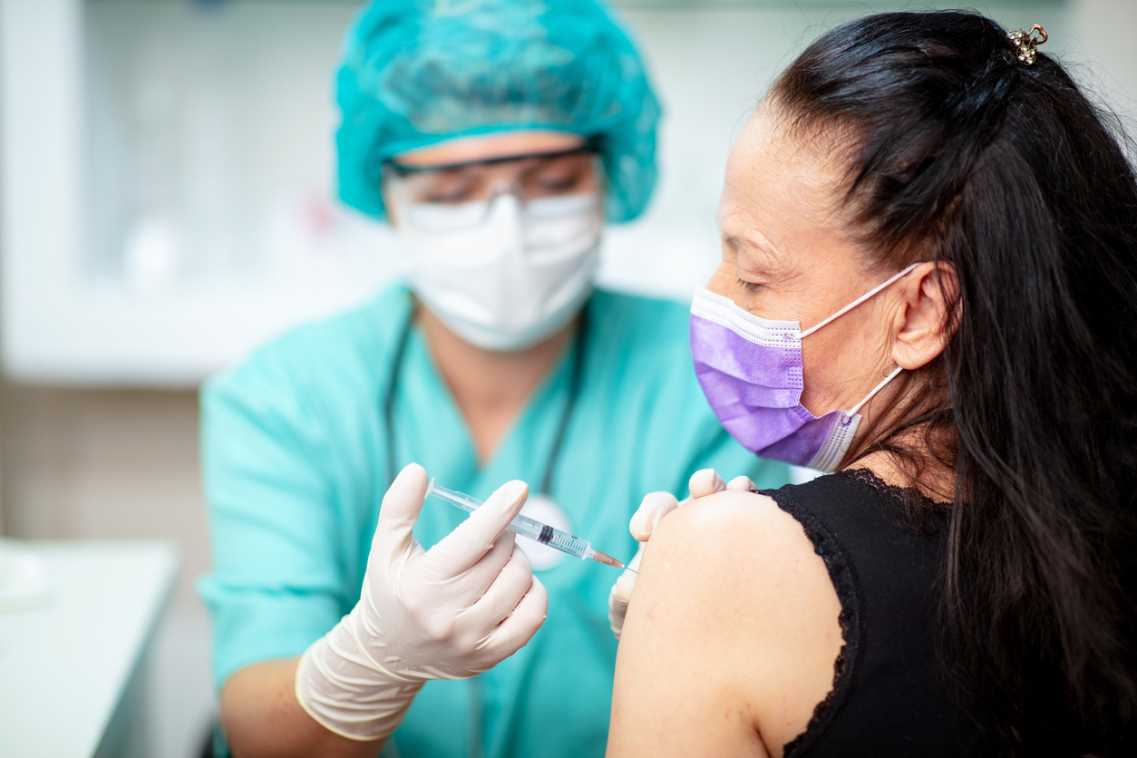 A middle-aged woman wearing a face mask receives a COVID vaccine from a female healthcare worker.