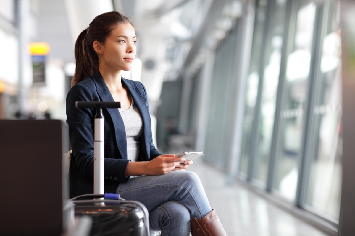 woman waiting in an airport sitting next to luggage while scrolling through a smartphone