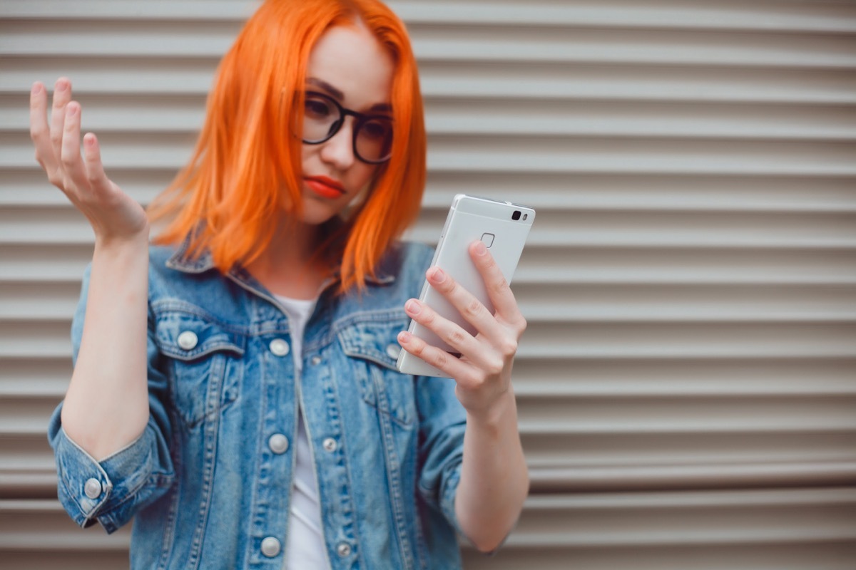 Woman standing outside and holding phone looking upset