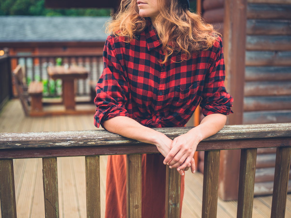 A young woman is relaxing on the porch of a log cabin in the country