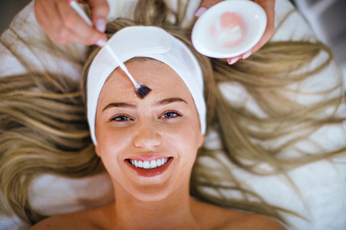 Unrecognizable beautician applying chemical peel on a young woman at beauty salon.