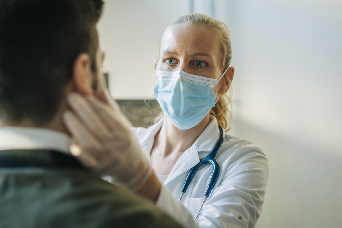 Doctor wearing surgical mask examining infected patient. Mature healthcare worker checking mid adult man. They are at pharmacy.