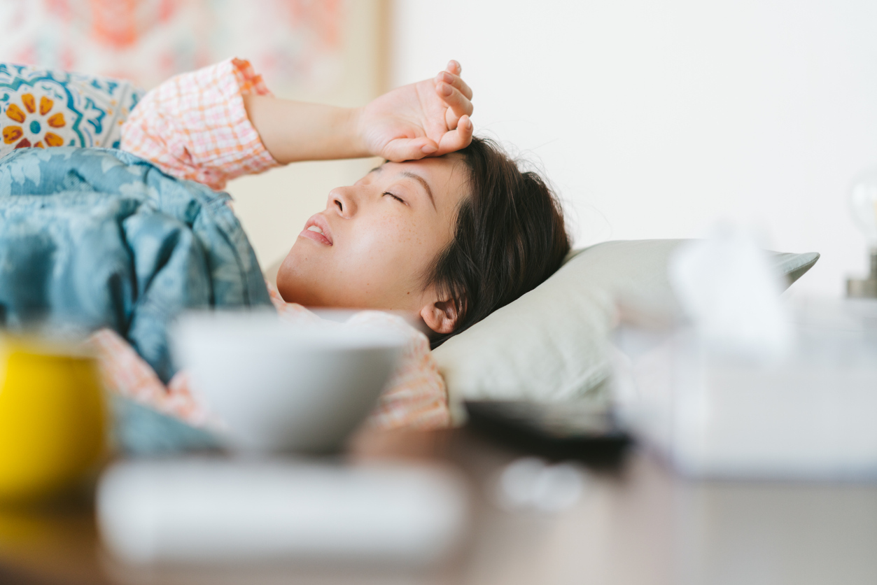 A sick asian woman lying on her sofa and covering her forehead with her hand