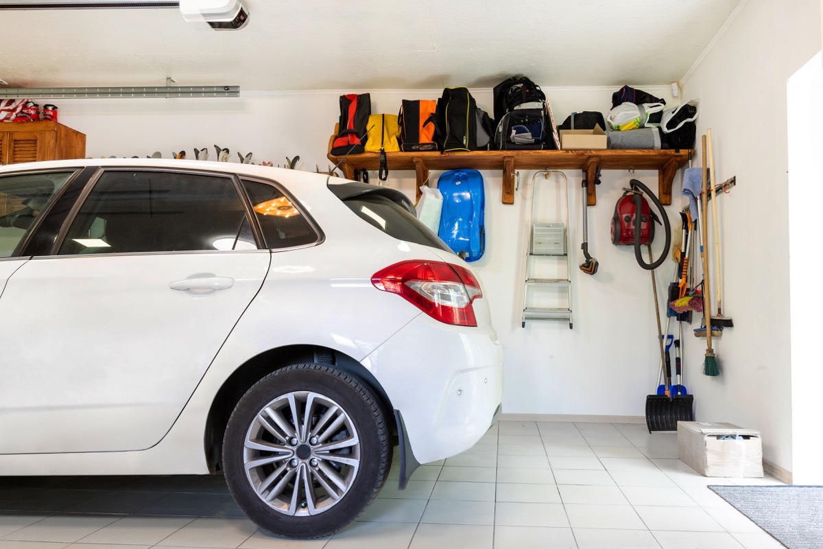 Home suburban car garage interior with wooden shelf , tools and equipment stuff storage warehouse on white wall indoors. Vehicle parked at house parking background