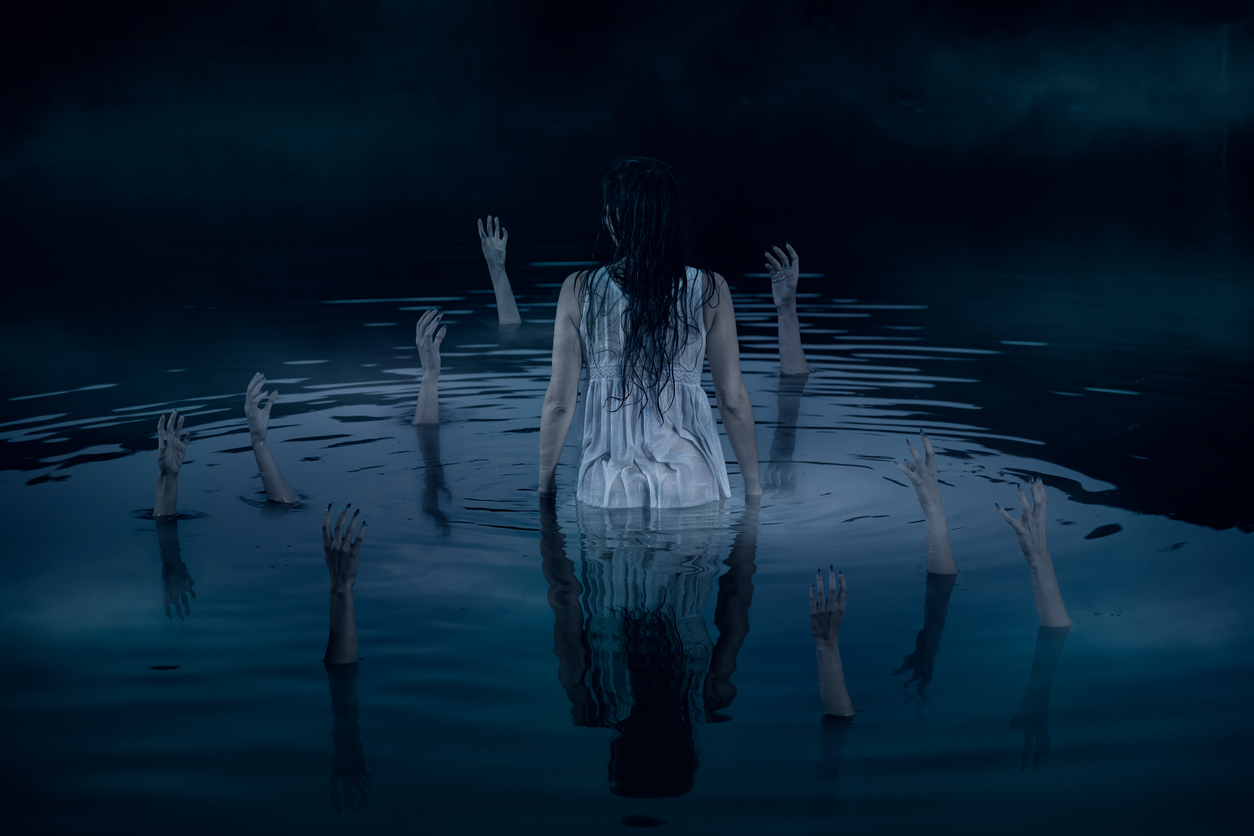 Hands sticking out of the water, reaching out to the woman in white night dress. Halloween horror concept.