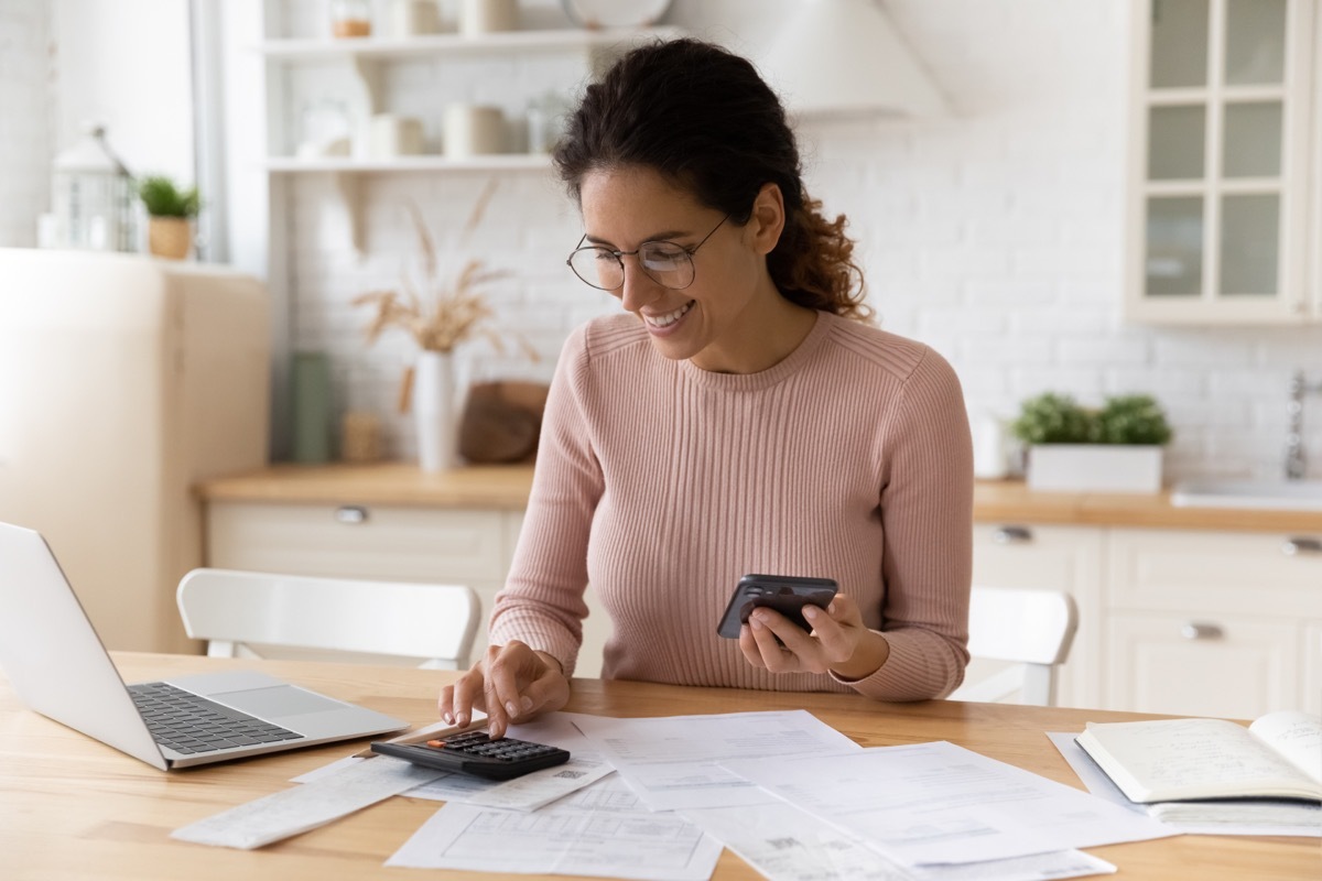 Young female work with financial papers at home count on calculator before paying taxes receipts online by phone. Millennial woman planning budget glad to find chance for economy saving money