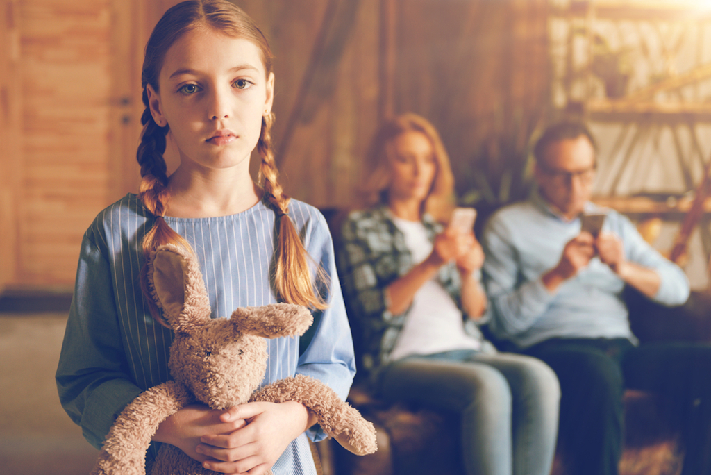 child looks upset as her parents check phones