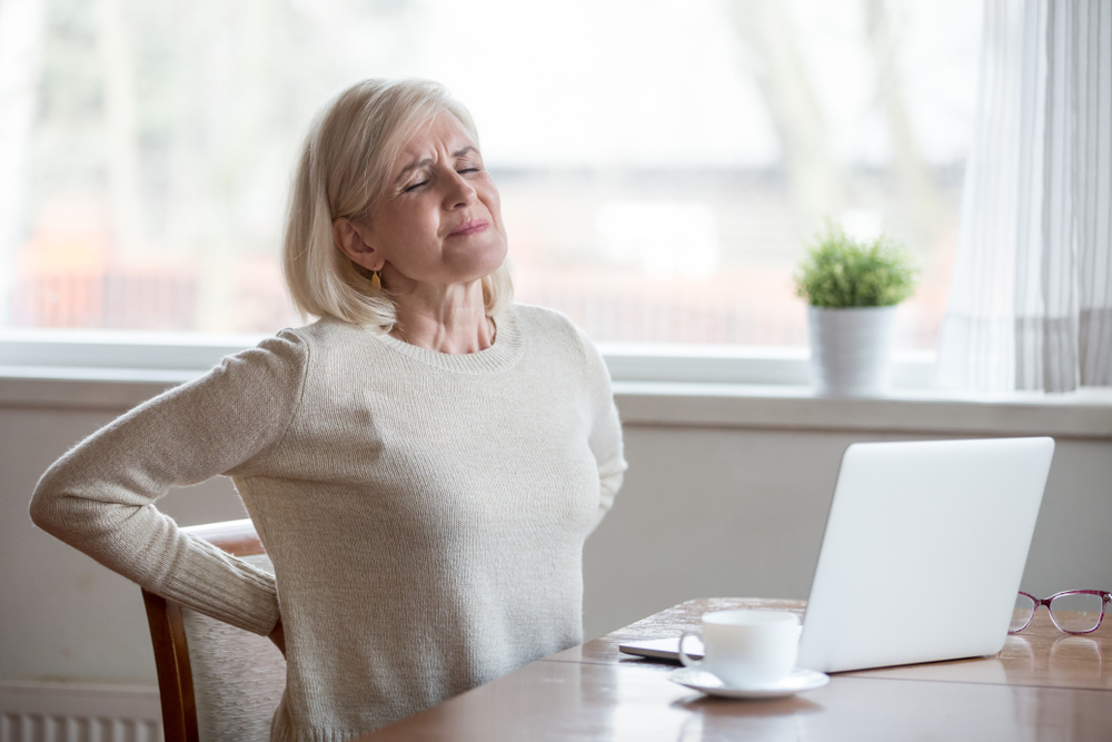 A senior woman sitting at a table holding her back in pain