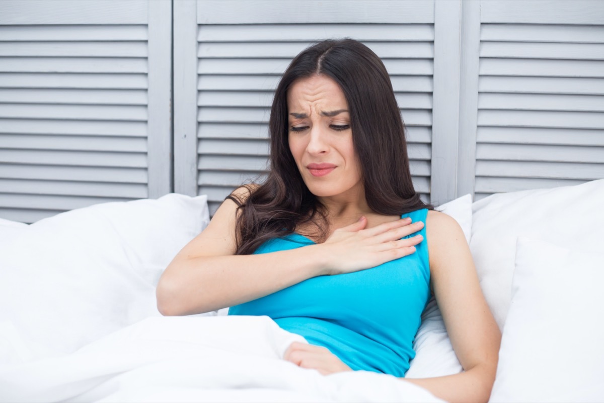 Woman lying in bed at home holding a hand to her chest by a sharp pain