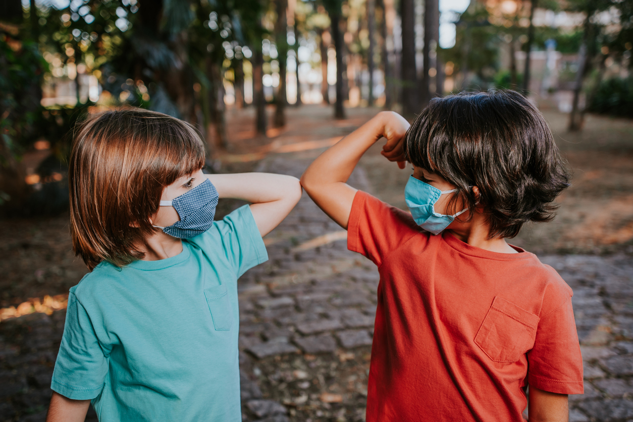 Two young boys wearing face masks bump elbows to say hello