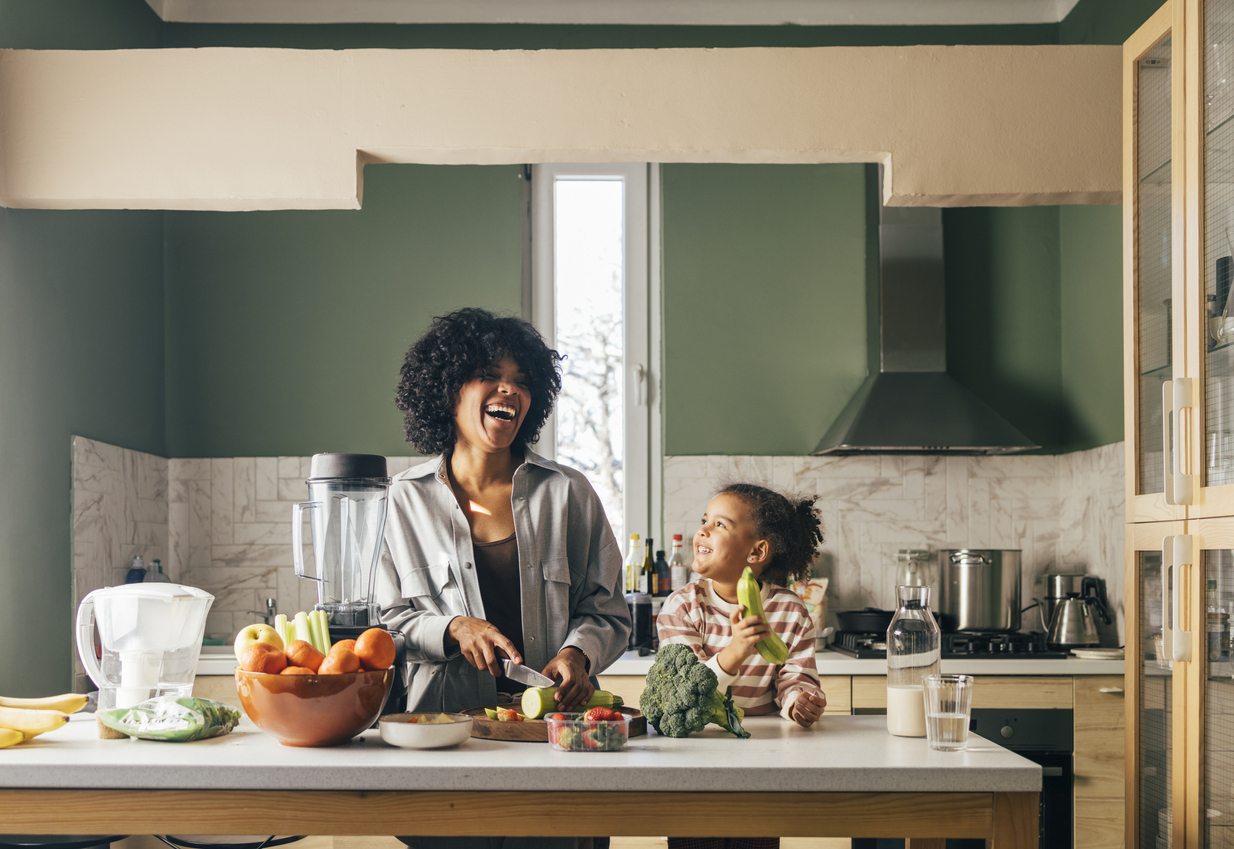 A happy mother having fun with her cute daughter while cutting vegetables.