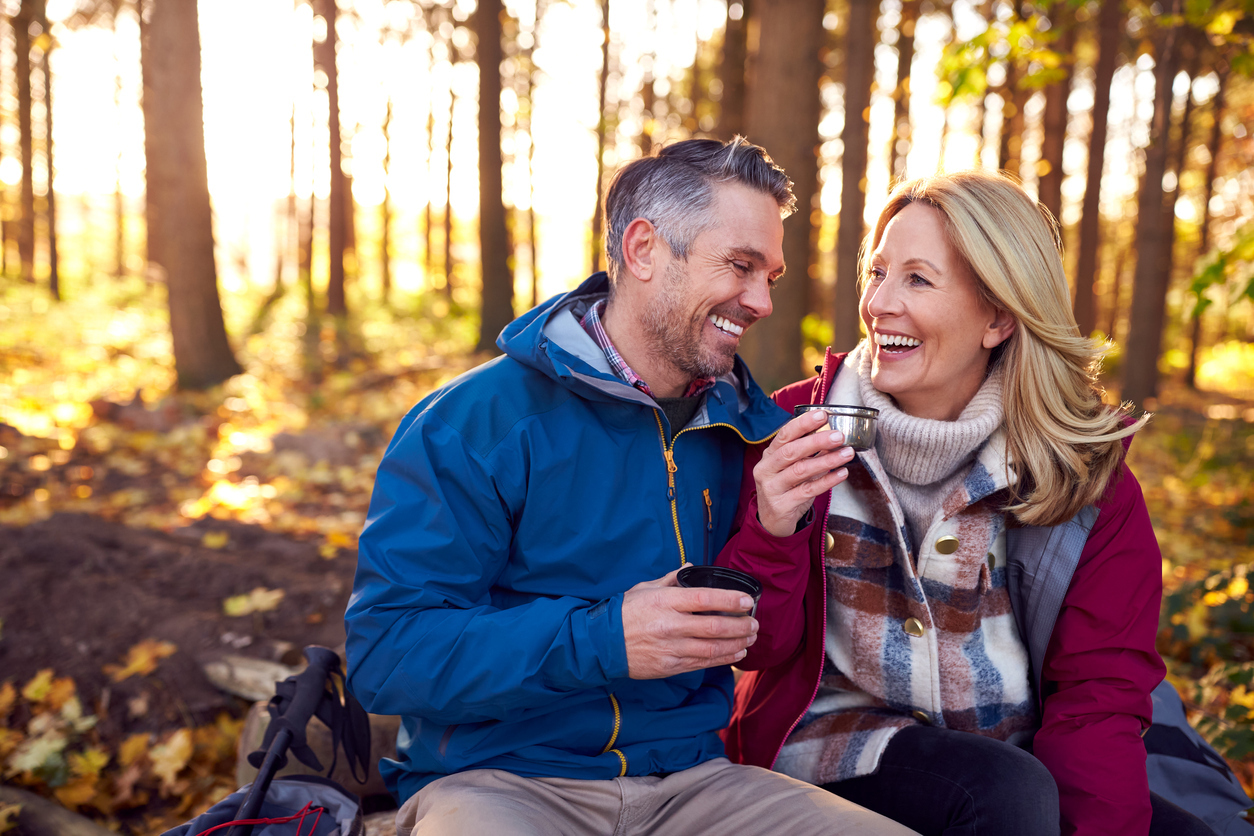 Couple sitting with hot drinks in the woods.