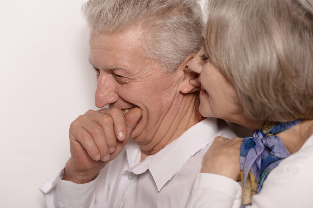 Older woman whispering into giggling old man's ear