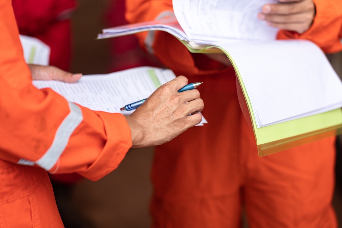 Action of operation supervisor is holding document paper during operational group meeting with other staffs. Industrial expertise occupation action photo. Close-up and selective focus at hand